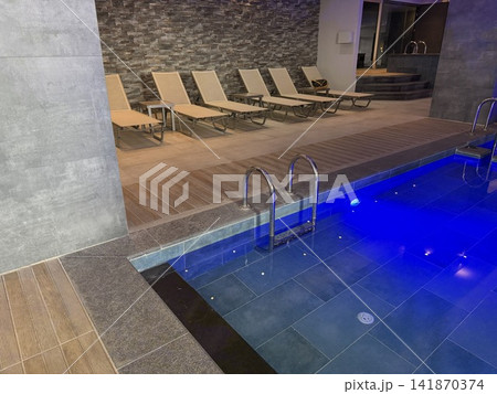 Indoor swimming pool with blue lighting and empty lounge chairs, suitable for a spa background Indoor swimming pool with blue lighting and empty lounge chairs, suitable for a spa background 141870374
