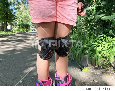 a little girl's legs in knee pads while roller skating. Protective equipment for outdoor activities a little girl's legs in knee pads while roller skating. Protective equipment for outdoor activities 141871341