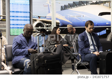 Waiting for flight, chatting and woman with man inside airport interior passing time. Getting acquainted, waiting for plane and girl with African traveler sharing stories about their planned holidays Waiting for flight, chatting and woman with man inside airport interior passing time. Getting acquainted, waiting for plane and girl with African traveler sharing stories about their planned holidays 141871757
