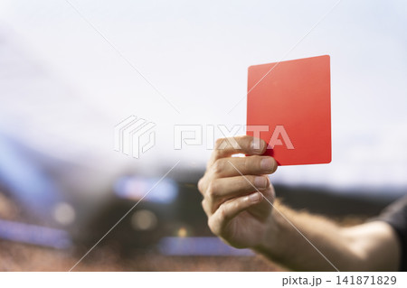 Close up of red card shown by referee as foul punishment during football match, dramatic sanction due to rules violation and unsportsmanlike conduct. Hand raising card with authority. 141871829