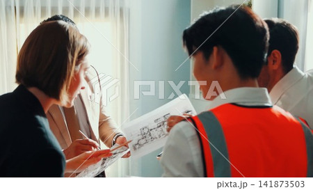 Top view of team inspect house model while manager hold blueprint. Alimentation. Top view of team inspect house model while manager hold blueprint. Alimentation. 141873503