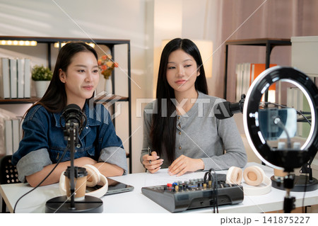 Two asian woman with microphone recording video podcast channel in studio. 141875227