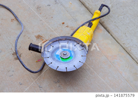 Power saw tool lies on cement slab at construction site, wear after work is done. Power saw tool lies on cement slab at construction site, wear after work is done. 141875579