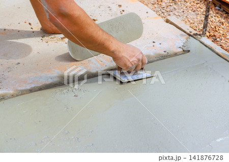 Contractor is smoothing fresh wet concrete with trowel on worksite Contractor is smoothing fresh wet concrete with trowel on worksite 141876728