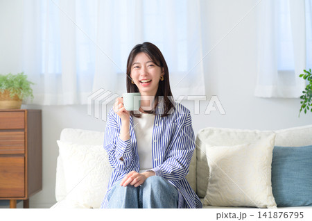 ソファでコーヒーを飲む笑顔の日本人女性 141876795