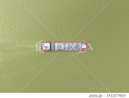 Long barge transports heavy goods through the murky river water in China leaving a wake behind it on a clear day with peaceful river currents Long barge transports heavy goods through the murky river water in China leaving a wake behind it on a clear day with peaceful river currents 141877603