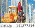 Red haired woman in leather clothes with motorcycle helmet looking at skyscrapers with copy space 141877816