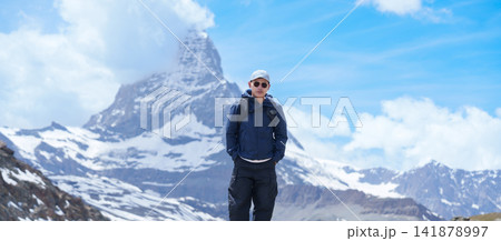 man Tourist Exploring Zermatt, Switzerland in summer. Happy Hiker Standing on Rock along Hiking Trail with Matterhorn, Swiss Alps, Famous Europe Landmark, Hiking Attraction and Travel Destination man Tourist Exploring Zermatt, Switzerland in summer. Happy Hiker Standing on Rock along Hiking Trail with Matterhorn, Swiss Alps, Famous Europe Landmark, Hiking Attraction and Travel Destination 141878997