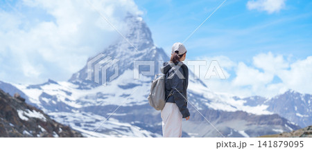 Woman Tourist Exploring Zermatt, Switzerland in summer. Happy Hiker Standing on Rock along Hiking Trail with Matterhorn, Swiss Alps, Famous Europe Landmark, Hiking Attraction and Travel Destination Woman Tourist Exploring Zermatt, Switzerland in summer. Happy Hiker Standing on Rock along Hiking Trail with Matterhorn, Swiss Alps, Famous Europe Landmark, Hiking Attraction and Travel Destination 141879095
