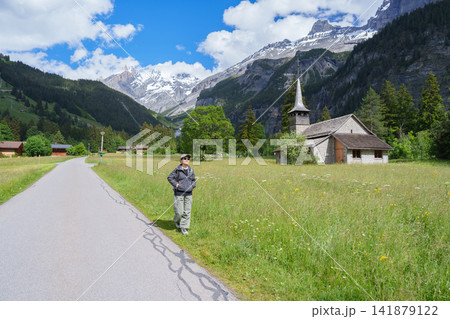 Woman Tourist Exploring Kandersteg Village, Switzerland in Summer. Traveler Walking Along a Scenic Village Trail with Traditional Swiss Wooden Chalet, Church, Wildflower Meadow and Stunning Swiss Alps Woman Tourist Exploring Kandersteg Village, Switzerland in Summer. Traveler Walking Along a Scenic Village Trail with Traditional Swiss Wooden Chalet, Church, Wildflower Meadow and Stunning Swiss Alps 141879122