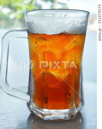 Refreshing iced tea in a transparent glass with ice over a blurred green tree background Refreshing iced tea in a transparent glass with ice over a blurred green tree background 141879574