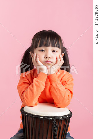 Cute Asian little girl playing drum, smiling child with percussion instrument on pink background, music education concept 141879665