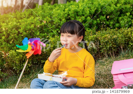 Asian little girl eating dessert in park, smiling happily, outdoor childhood lifestyle for leisure, picnic and healthy growth concept Asian little girl eating dessert in park, smiling happily, outdoor childhood lifestyle for leisure, picnic and healthy growth concept 141879969
