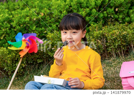 Asian little girl eating dessert in park, smiling happily, outdoor childhood lifestyle for leisure, picnic and healthy growth concept Asian little girl eating dessert in park, smiling happily, outdoor childhood lifestyle for leisure, picnic and healthy growth concept 141879970