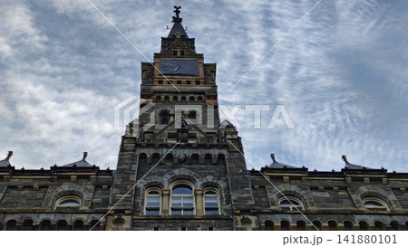 The majestic stone tower of Healy Hall at Georgetown University reaches skyward. The historic neo-Gothic facade is adorned with a vintage clock and spire The majestic stone tower of Healy Hall at Georgetown University reaches skyward. The historic neo-Gothic facade is adorned with a vintage clock and spire 141880101
