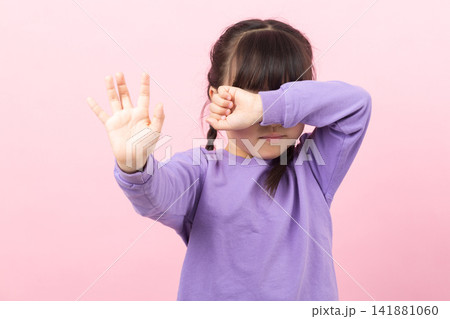 Little girl covering her face with an arm and reaching out a hand to say stop. Little girl covering her face with an arm and reaching out a hand to say stop. 141881060