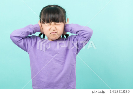 Frustrated little girl covering her ears with hands and closing eyes on a turquoise background. 141881089