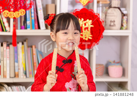 Smiling Asian Child Holding Traditional Rice Crust Snacks for Spring Festival,The text on the pendant hanging at the back reads: "Happy New Year." 141881248
