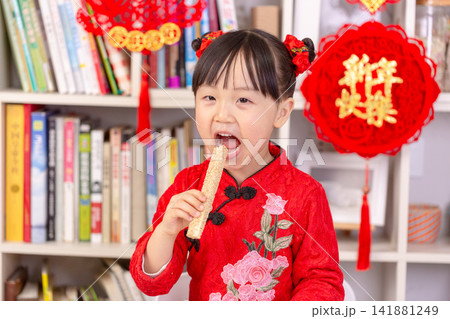 Smiling Asian Child Holding Traditional Rice Crust Snacks for Spring Festival,The text on the pendant hanging at the back reads: "Happy New Year." 141881249