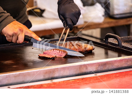 大きな鉄板の上でシェフの手により切り分けられていく厚切りステーキ肉 141881388