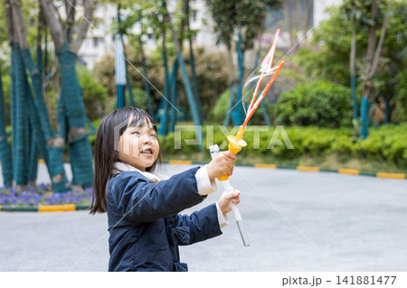 Joyful little girl holding a bubble wand and laughing with huge soap bubbles in the garden. 141881477