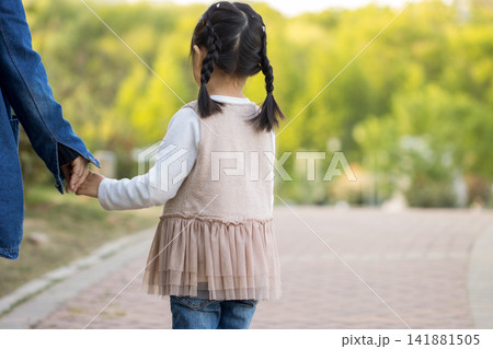 Back view of a mother and daughter holding hands and walking together in a sunny park. Back view of a mother and daughter holding hands and walking together in a sunny park. 141881505