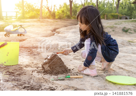 Child building a mud castle on the riverbank using toy shovel and bucket. Child building a mud castle on the riverbank using toy shovel and bucket. 141881576