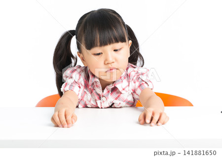 Pouting girl sitting at a desk next to a stack of books and an alarm clock. Pouting girl sitting at a desk next to a stack of books and an alarm clock. 141881650