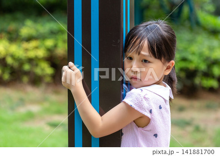 Shy little girl hiding behind a pole and peeking, social anxiety concept Shy little girl hiding behind a pole and peeking, social anxiety concept 141881700