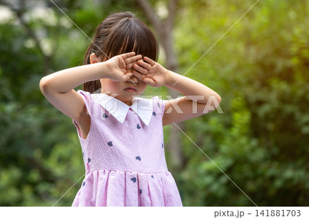 A lonely and heartbroken Asian little girl outdoors, covering her eyes with both hands. A lonely and heartbroken Asian little girl outdoors, covering her eyes with both hands. 141881703