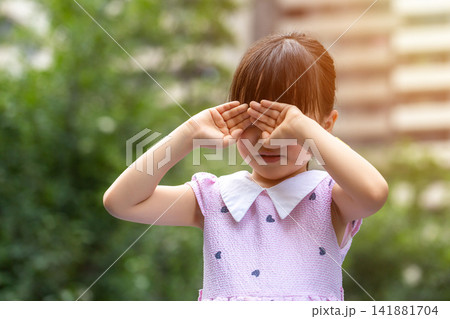 A lonely and heartbroken Asian little girl outdoors, covering her eyes with both hands. A lonely and heartbroken Asian little girl outdoors, covering her eyes with both hands. 141881704