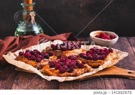 Crispy puff pastry with raspberries on parchment paper on the table Crispy puff pastry with raspberries on parchment paper on the table 141882678