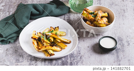 Appetizing baked zucchini strips on a plate and a bowl of sauce on the table web banner Appetizing baked zucchini strips on a plate and a bowl of sauce on the table web banner 141882701