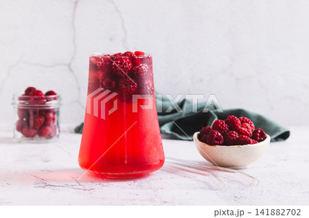 Cold raspberry compote in a glass and berries in a bowl on the table 141882702