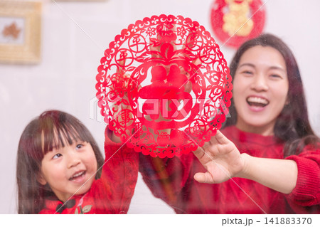 Happy Asian Mother and Daughter Holding Chinese New Year Decoration at Home,The text on the New Year decoration reads: "Fu."(Good Blessings) 141883370