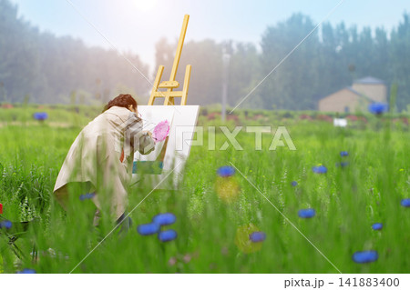 Young girl student painting on a canvas in a vast green meadow during art class. Young girl student painting on a canvas in a vast green meadow during art class. 141883400