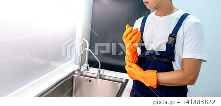 Asian male housekeeper putting on orange rubber gloves preparing himself for cleaning kitchen 141883822