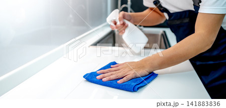 Male housekeeper hand holding spray bottle while wiping microfiber cloth on white countertop Male housekeeper hand holding spray bottle while wiping microfiber cloth on white countertop 141883836