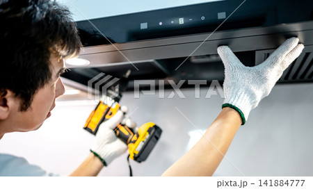 Asian male technician using electric screwdriver fixing extractor motor in cooker hood 141884777