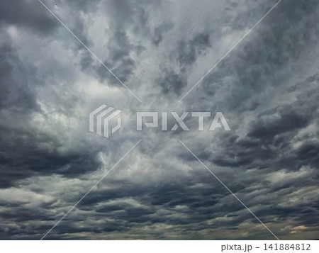 Dramatic dark stormy clouds fill the sky above a landscape, signaling upcoming weather changes during the daytime Dramatic dark stormy clouds fill the sky above a landscape, signaling upcoming weather changes during the daytime 141884812