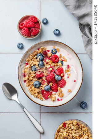 Natural greek yogurt with granola, blueberry and raspberry in a bowl on a blue tile background 141885040