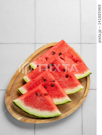 Summer concept of juicy and ripe slices of red watermelon with seeds on a wooden plate Summer concept of juicy and ripe slices of red watermelon with seeds on a wooden plate 141885069