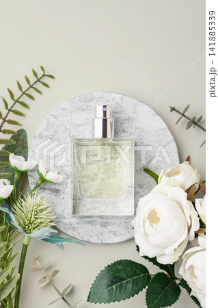 Glass perfume bottle on marble tray with white roses and green leaves decoration on beige background. copy space Glass perfume bottle on marble tray with white roses and green leaves decoration on beige background. copy space 141885339