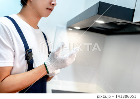 Asian male maintenance worker putting on protective gloves while fixing the cooker hood 141886053