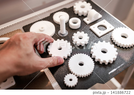 Hand arranging white 3d printed gears and parts on a work table, product prototyping, engineering design, and manufacturing concept Hand arranging white 3d printed gears and parts on a work table, product prototyping, engineering design, and manufacturing concept 141886722