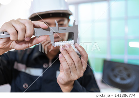 Factory worker measuring a plastic part with a caliper during quality inspection Factory worker measuring a plastic part with a caliper during quality inspection 141886774