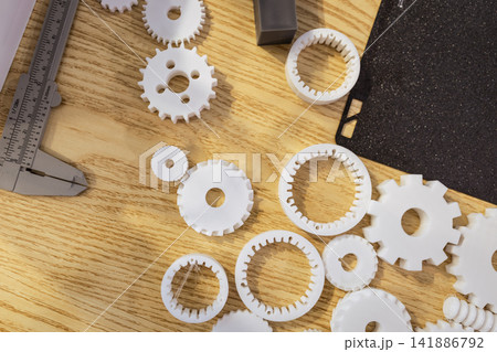 White plastic gear prototypes and measuring tools on a wooden workbench, seen from above White plastic gear prototypes and measuring tools on a wooden workbench, seen from above 141886792