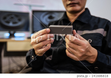 Close up of a technician holding a small metal part in a workshop, with blurred machinery in the background Close up of a technician holding a small metal part in a workshop, with blurred machinery in the background 141886818