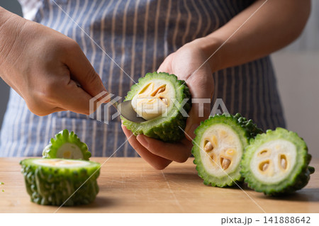 Woman hands removing seeds from a fresh bitter gourd using a spoon, preparing food ingredient Woman hands removing seeds from a fresh bitter gourd using a spoon, preparing food ingredient 141888642