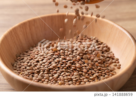 Raw green lentils pouring into a wooden bowl, high protein plant-based food and meat alternative Raw green lentils pouring into a wooden bowl, high protein plant-based food and meat alternative 141888659